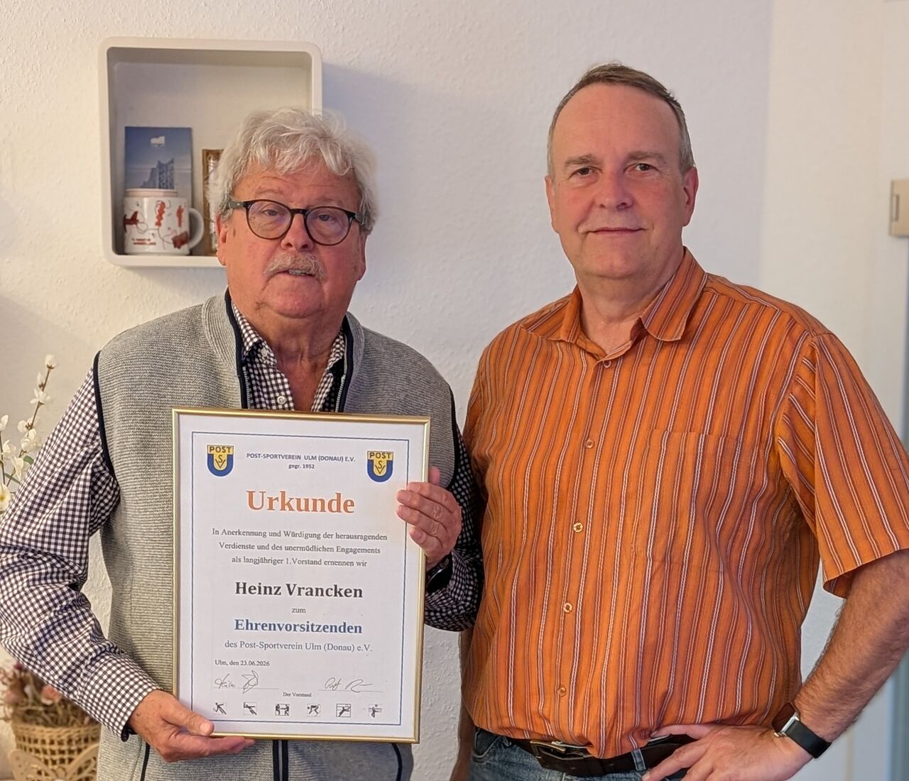 Zwei Männer stehen nebeneinander, einer hält die gerahmte Urkunde zur Ernennung von Heinz Vrancken zum Ehrenvorsitzenden des Post-Sportverein Ulm (Donau) e.V.